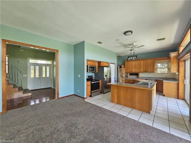 Kitchen featuring appliances with stainless steel finishes, a kitchen island, ceiling fan, decorative light fixtures, and light colored carpet