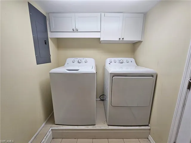Washroom featuring cabinets, light tile patterned flooring, electric panel, and washer and dryer