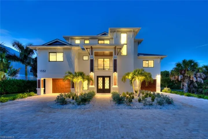 Front exterior at twilight featuring modern architecture, paver driveway, and tropical landscaping