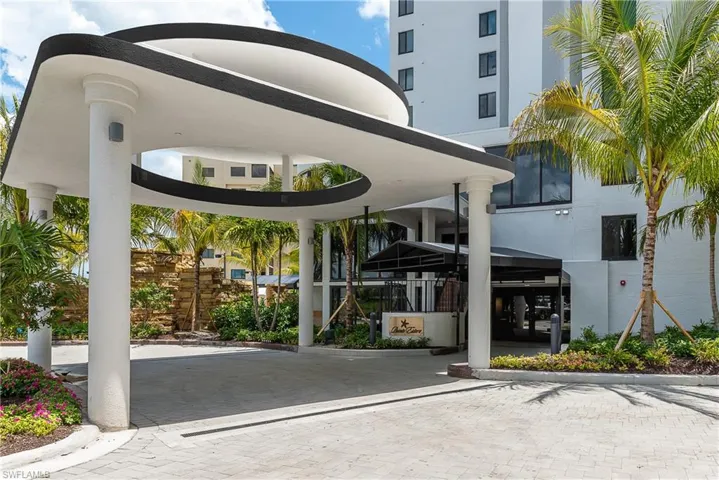 Covered arrival area with large columns, paver driveway, and lush landscaping