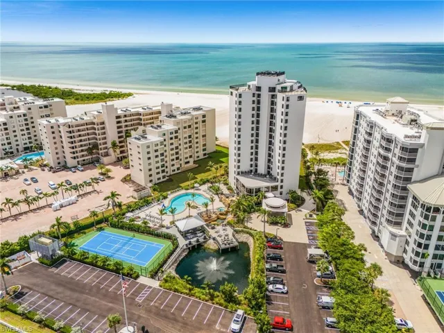 Expansive coastal property featuring multiple residential buildings, a large swimming pool, a tennis court, a decorative pond with a fountain, and direct beach access