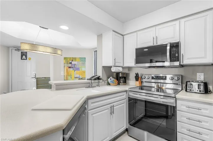 White cabinetry, stainless steel appliances, solid surface countertops, a built-in sink, and a linear pendant light fixture