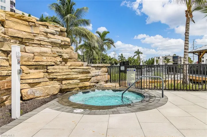 Outdoor spa with stone surround, paver and tile decking, and metal safety railing