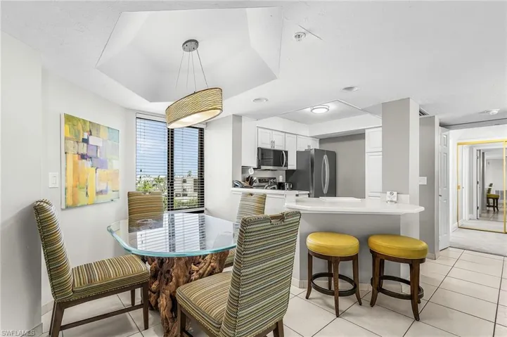 Bright dining area featuring a tray ceiling with a suspended light fixture, tile flooring, and a kitchen pass-through with a breakfast bar