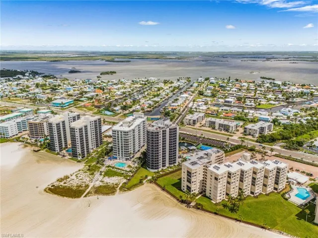 Coastal setting featuring direct beach access, multiple high-rise buildings, canals, and a large body of water in the background