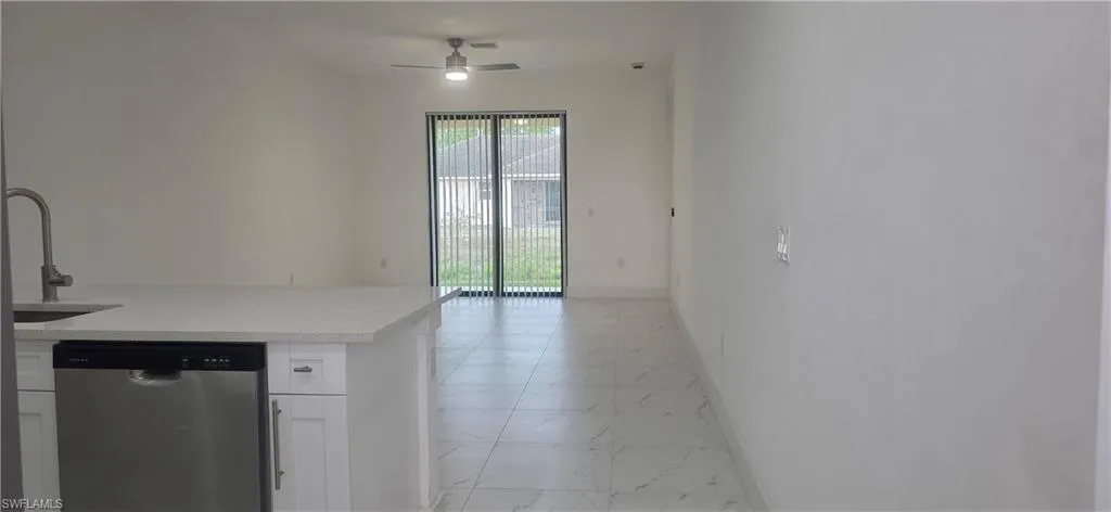 Kitchen featuring stainless steel dishwasher, white cabinets, light stone countertops, a ceiling fan, and light marble finish floors