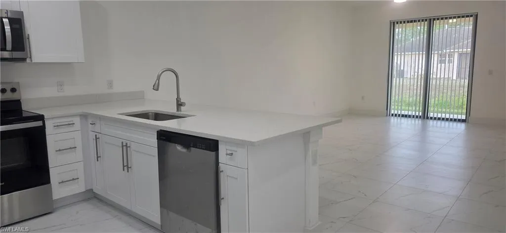 Kitchen with light marble finish flooring, appliances with stainless steel finishes, white cabinets, light stone counters, and a peninsula