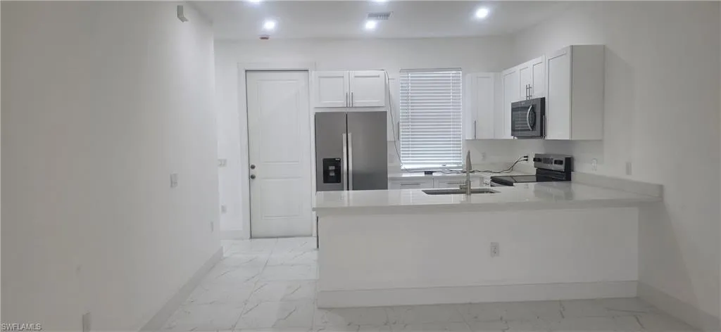 Kitchen featuring light stone counters, stainless steel appliances, white cabinets, light marble finish flooring, and a peninsula