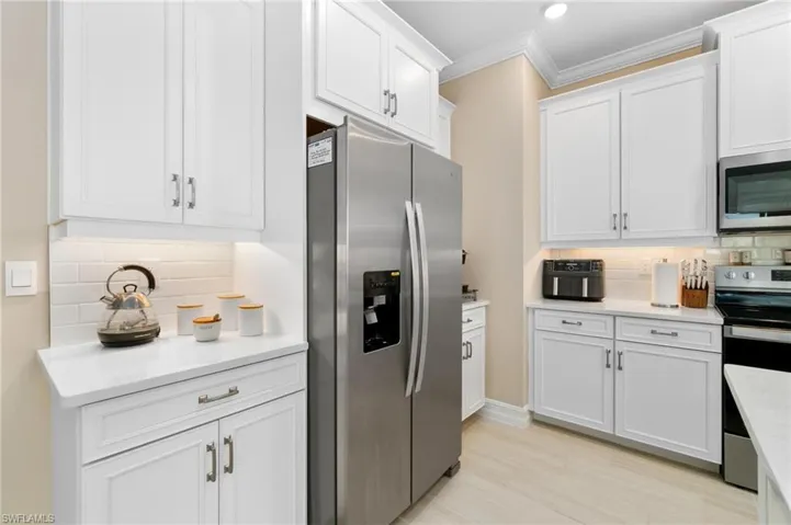 Kitchen with tasteful backsplash, stainless steel appliances, white cabinetry, and crown molding
