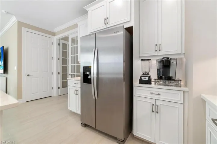Kitchen featuring stainless steel fridge with ice dispenser, white cabinetry, crown molding, backsplash, and light stone countertops
