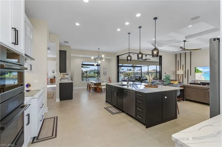 Kitchen with a spacious island, coffered ceiling, white cabinetry, decorative light fixtures, and ceiling fan with notable chandelier