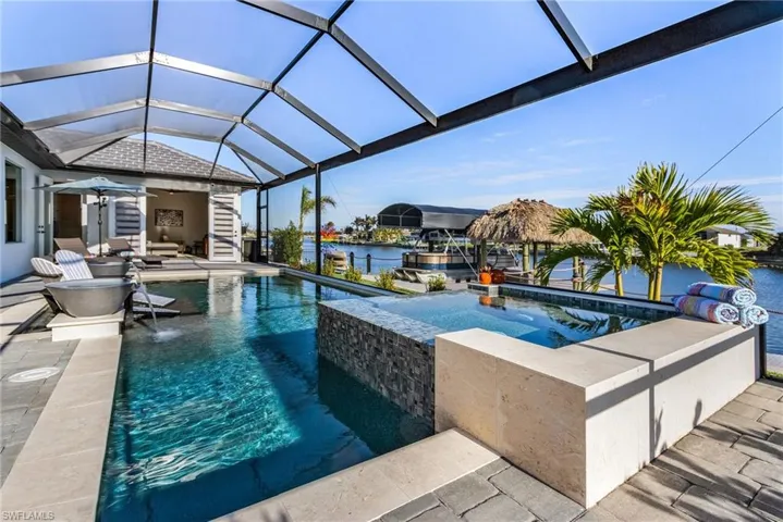 View of pool featuring pool water feature, a water view, a hot tub, glass enclosure, and a patio