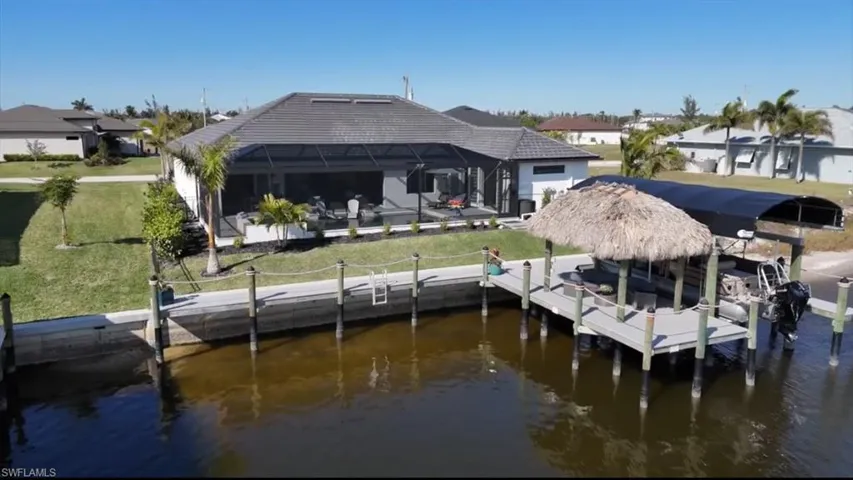 View of dock with a water view, glass enclosure, and a lawn