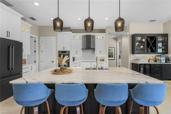 Kitchen with a spacious island, sink, wall chimney range hood, and high end black fridge