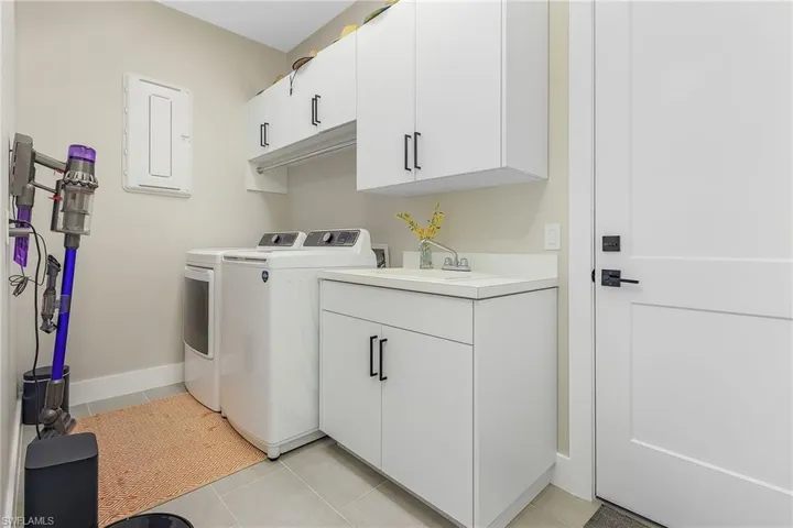 Clothes washing area with separate washer and dryer, light tile patterned floors, sink, and cabinets