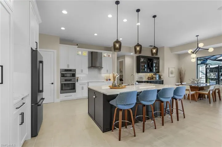 Kitchen with double oven, white cabinets, a large island with sink, hanging light fixtures, and wall chimney exhaust hood