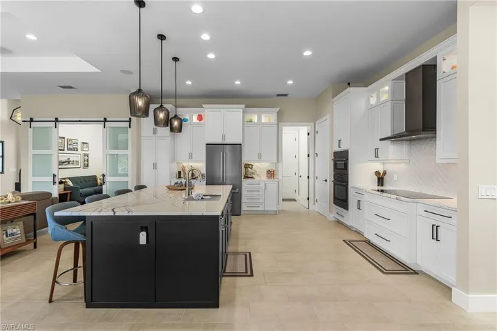 Kitchen featuring white cabinets, a barn door, wall chimney exhaust hood, and a center island with sink