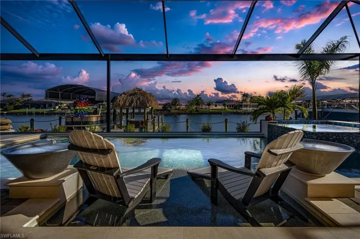 Pool at dusk with a water view, an in ground hot tub, and a lanai