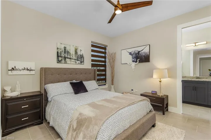 Bedroom featuring ceiling fan, sink, light tile patterned floors, and ensuite bath