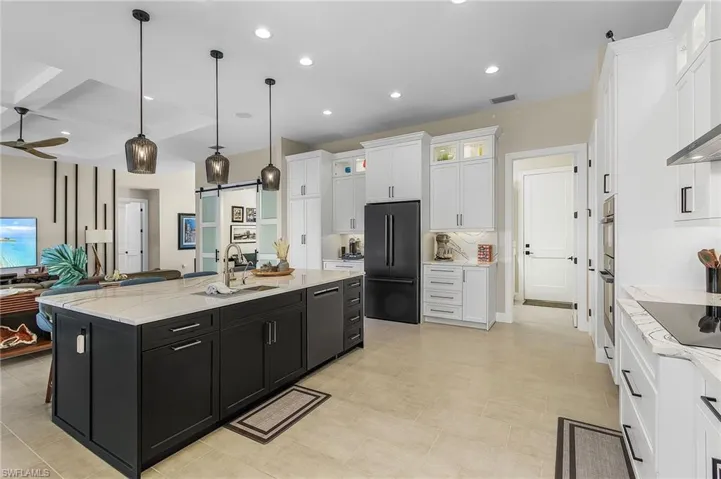 Kitchen featuring a large island, pendant lighting, white cabinetry, black appliances, and a barn door