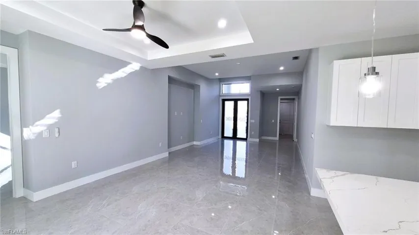 Empty room with ceiling fan, a raised ceiling, light marble finish floors, french doors, and recessed lighting