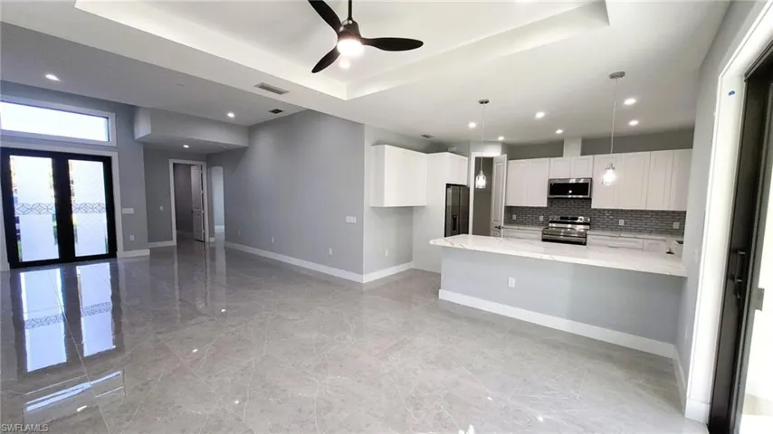 Kitchen featuring a peninsula, white cabinets, appliances with stainless steel finishes, light stone counters, and decorative light fixtures