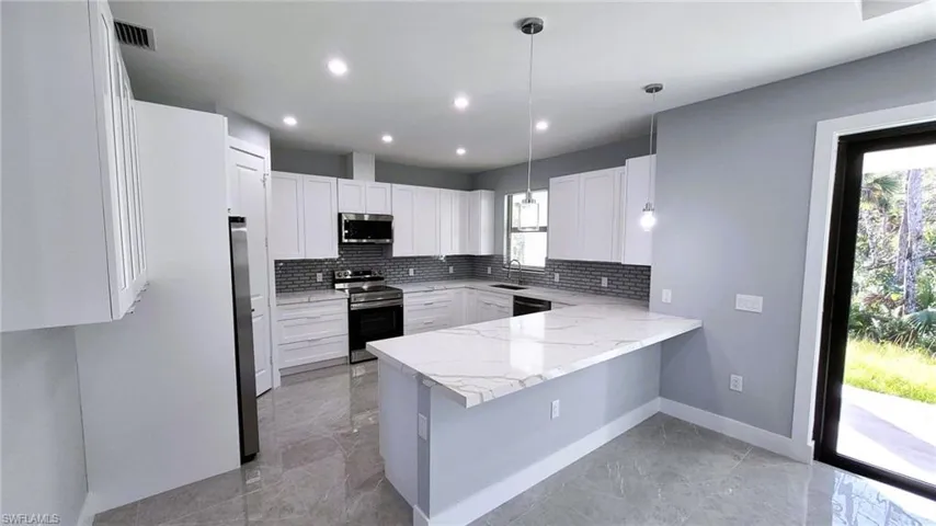 Kitchen featuring a peninsula, stainless steel appliances, decorative light fixtures, white cabinets, and tasteful backsplash
