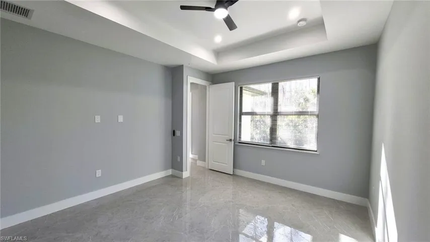 Unfurnished bedroom with a tray ceiling, light marble finish floors, and ceiling fan