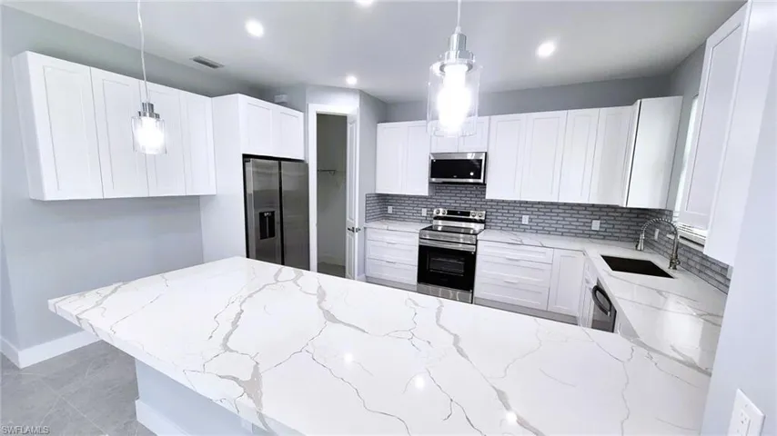 Kitchen featuring a peninsula, light stone counters, appliances with stainless steel finishes, decorative light fixtures, and white cabinetry