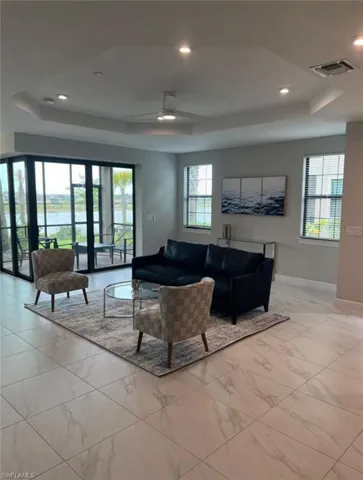 Living room with a tray ceiling, ceiling fan, recessed lighting, a water view, and light marble finish flooring