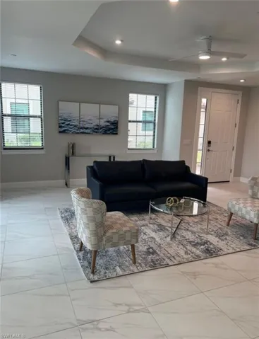 Living room with ceiling fan, a raised ceiling, light marble finish flooring, and recessed lighting