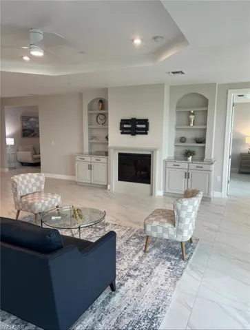 Living area with built in shelves, light marble finish flooring, a raised ceiling, and a glass covered fireplace