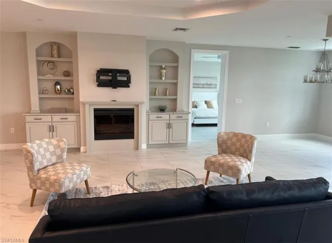 Living room with a raised ceiling, built in features, light marble finish floors, a glass covered fireplace, and suspended lighting
