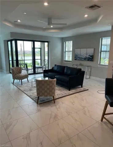 Living room featuring a tray ceiling, a ceiling fan, light marble finish flooring, and recessed lighting