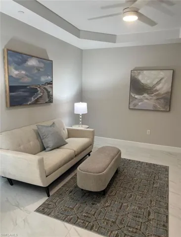 Living area with marble look tile flooring, a ceiling fan, and a tray ceiling