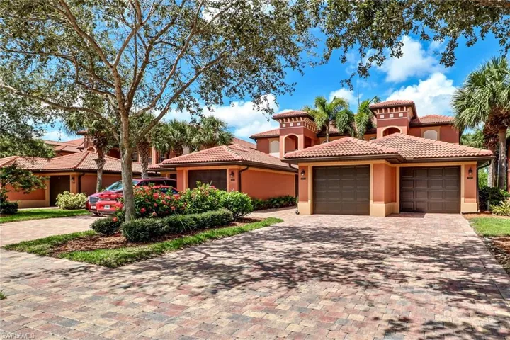 Stucco exterior featuring terracotta tile roofing, multi-level architectural detailing, and dual-car garage bays, accented by a paved stone driveway