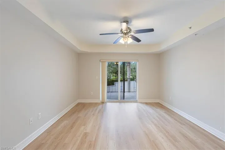 Unfurnished room with a tray ceiling, light wood-style flooring, and a ceiling fan