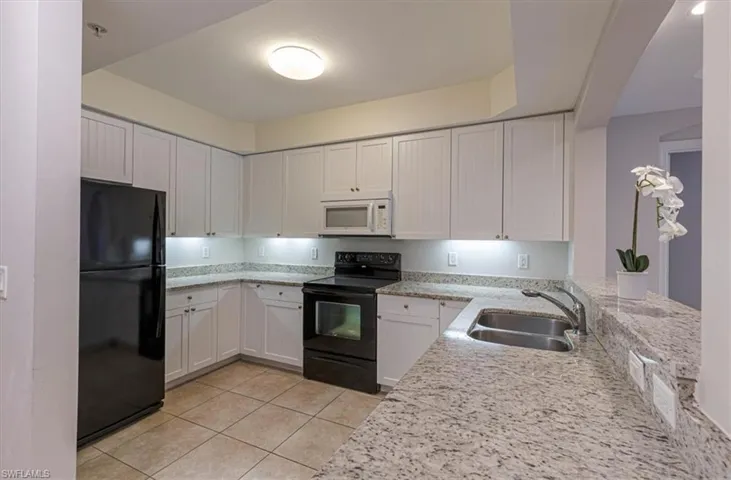 Kitchen with black appliances, light stone countertops, light tile patterned flooring, and white cabinetry