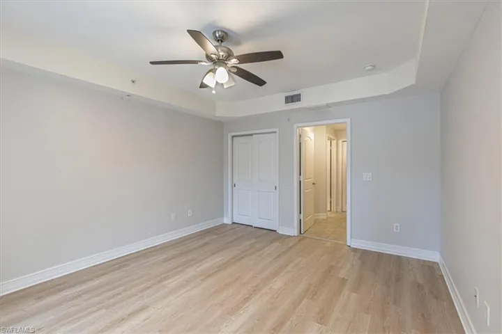 Unfurnished bedroom featuring light wood finished floors, a raised ceiling, a closet, and ceiling fan