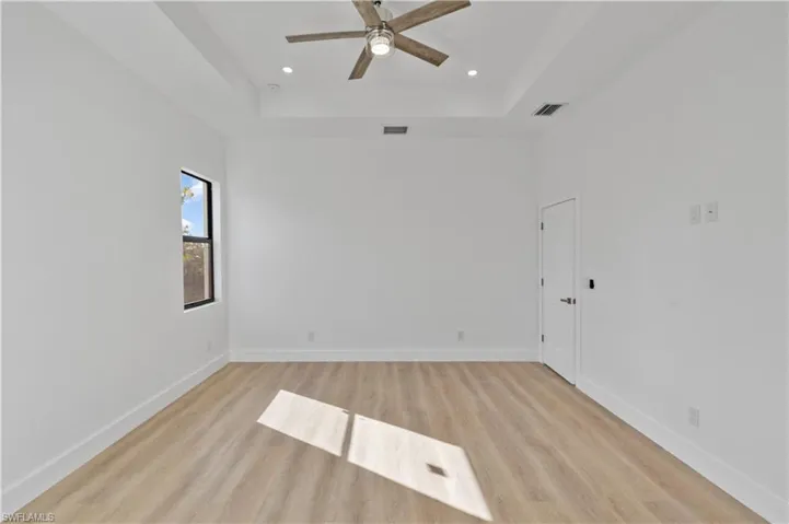 Empty room featuring light wood-style floors, a tray ceiling, ceiling fan, and recessed lighting