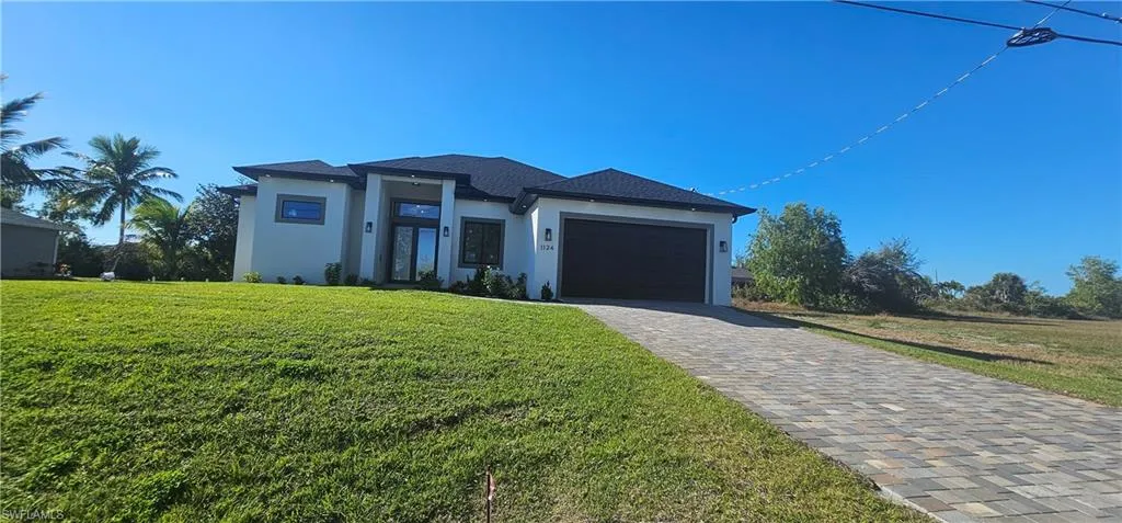Prairie-style home with stucco siding, decorative driveway, a front lawn, and roof with shingles