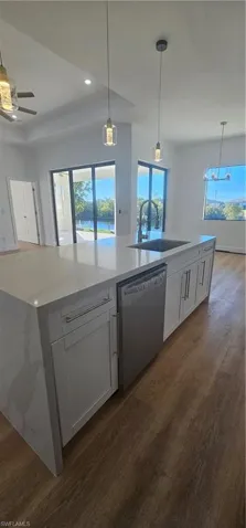 Kitchen featuring open floor plan, hanging light fixtures, white cabinets, an island with sink, and wall chimney range hood