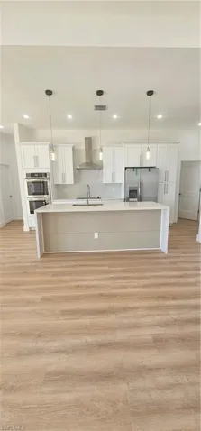 Unfurnished living room with a chandelier, light wood-style flooring, a ceiling fan, a raised ceiling, and recessed lighting