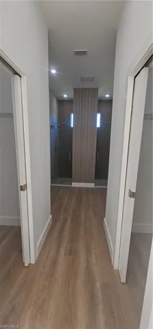 Kitchen featuring light stone counters, white cabinetry, light wood-style flooring, appliances with stainless steel finishes, and wall chimney range hood