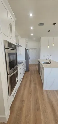 Kitchen with stainless steel appliances, white cabinets, wall chimney range hood, decorative light fixtures, and light wood finished floors