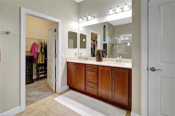 Bathroom with a walk in closet, a shower stall, double vanity, and light tile patterned flooring