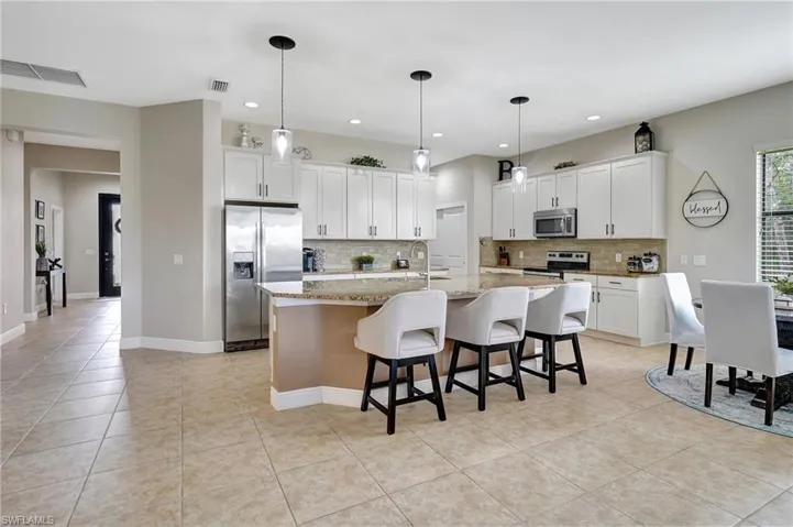 Kitchen with a kitchen breakfast bar, pendant lighting, stainless steel appliances, light tile patterned floors, and tasteful backsplash