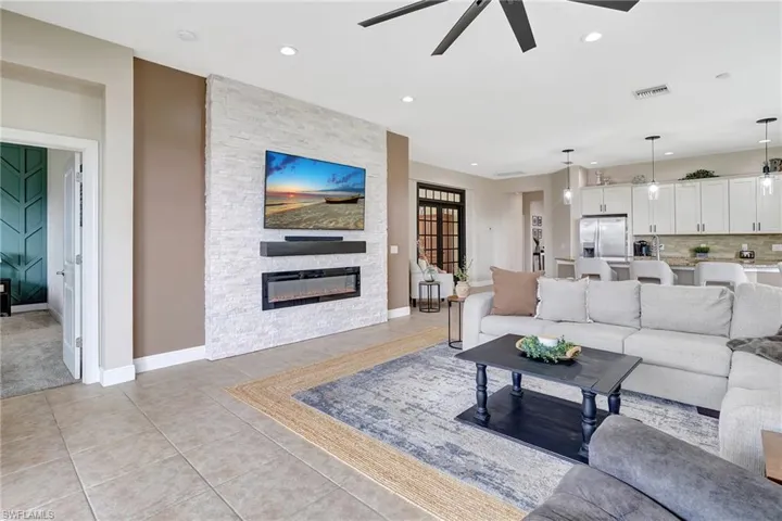 Living room with light tile patterned floors, ceiling fan, a stone fireplace, and recessed lighting