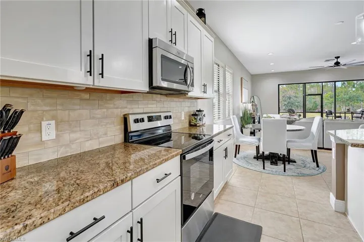 Kitchen featuring appliances with stainless steel finishes, white cabinetry, tasteful backsplash, light tile patterned floors, and a ceiling fan