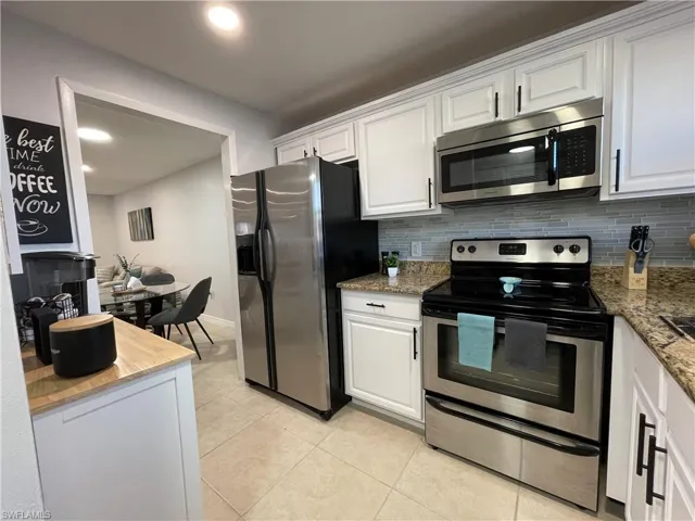 Kitchen with stainless steel appliances, white cabinets, backsplash, light stone counters, and light tile patterned floors